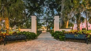 A paved pathway leading to a gated entrance with benches on either side. - East Riverside Downtown Bungalow (Port Richey)