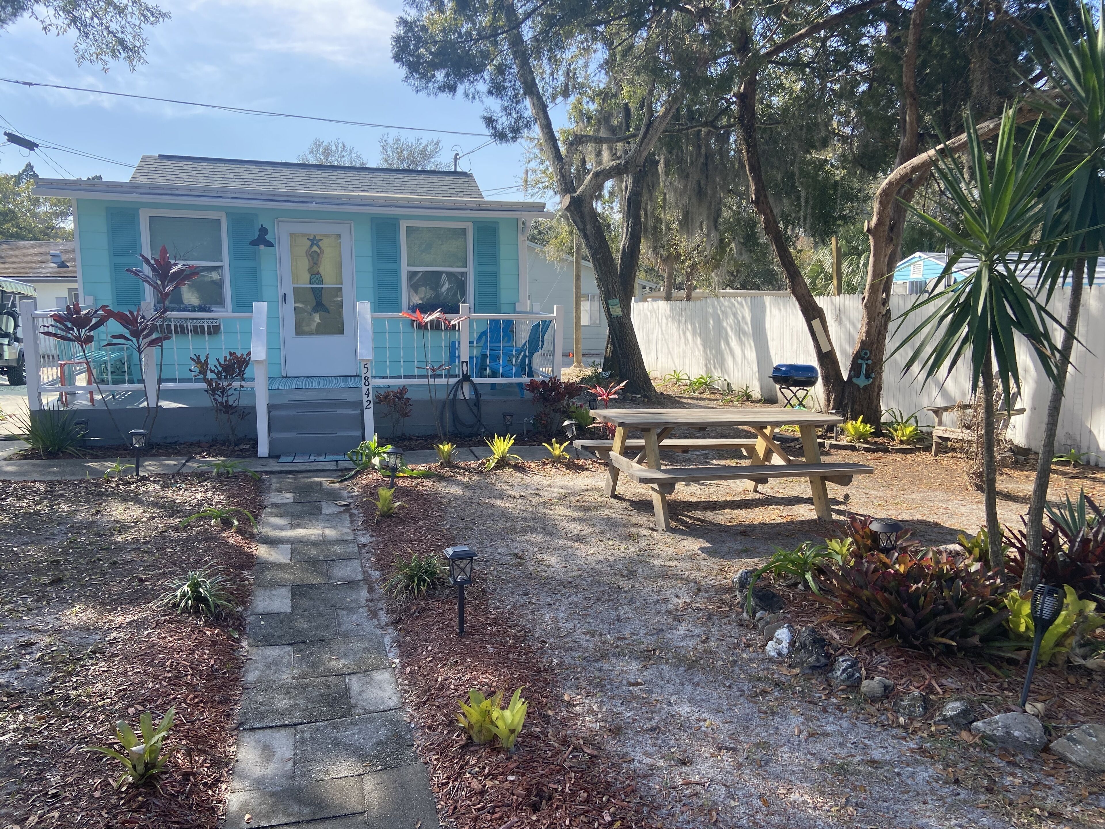 A small house with a front porch, a wooden bench, and a barbecue grill.