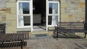 A stone building with an arched entrance, two benches outside, and a visible interior with a bed. - Robin Cottage Nr Rothbury (Weldon Bridge, near Rothbury)