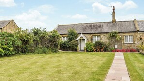 A stone cottage with a thatched roof, a small garden, and a paved pathway leading to the entrance.