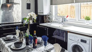 Una cucina moderna con lavatrice integrata, un tavolo da pranzo per due persone e una finestra vista un recinto di legno.