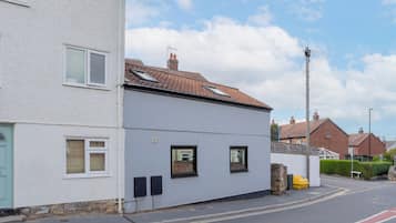 A two-story residential building with a flat roof, a visible chimney, and a small front garden.