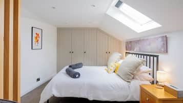 A bedroom with a skylight, a bed with pillows, a nightstand, and a framed picture on the wall.