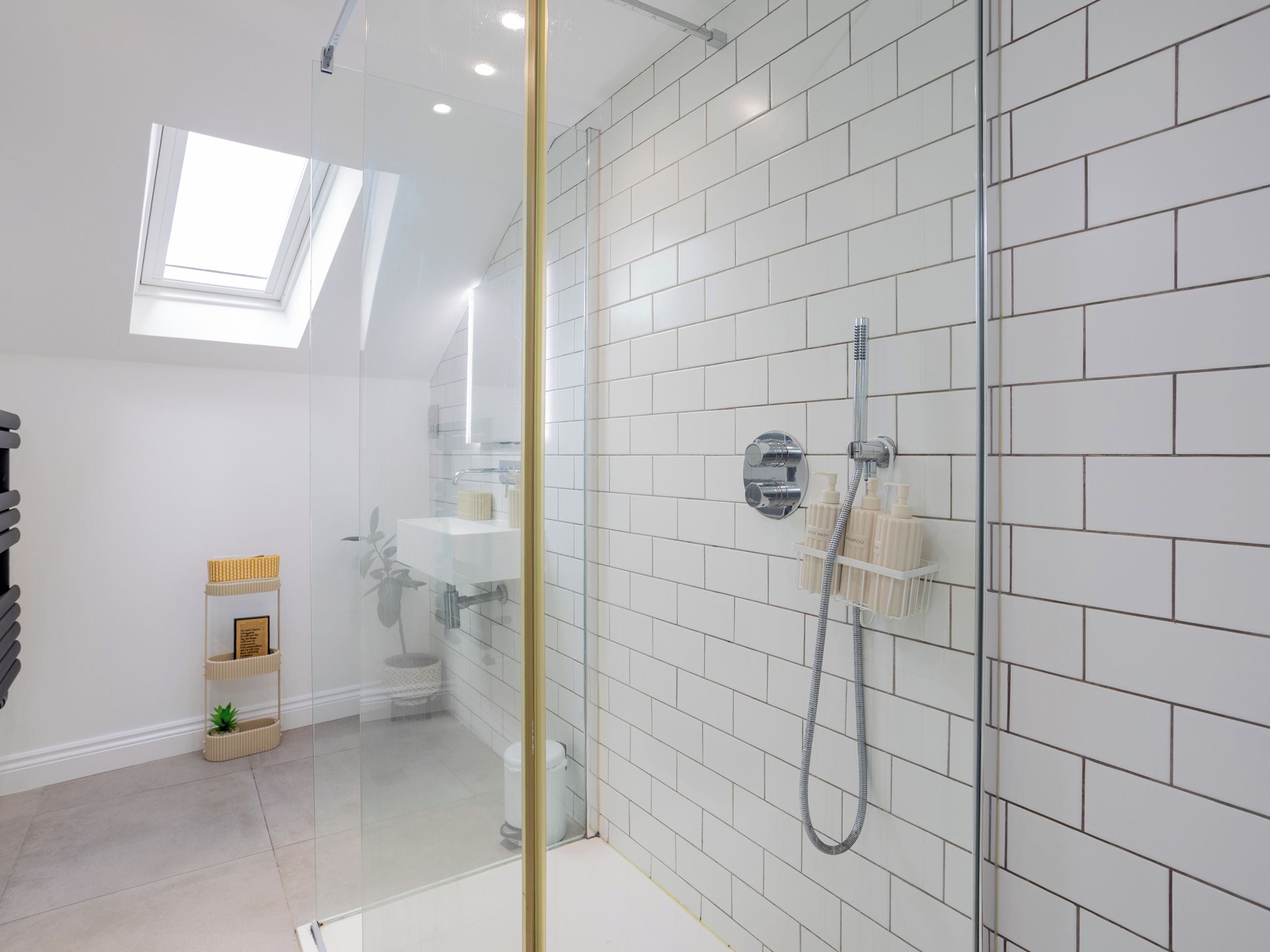 A modern bathroom with a glass-enclosed shower, white tiled walls, and a skylight.