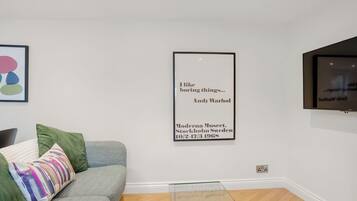 A modern living room with a grey sofa, a glass coffee table, and a framed quote on the wall.