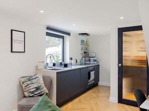 A modern kitchen with a built-in oven, a coffee machine, and a microwave. There is a window above the sink and a door with a textured glass panel.