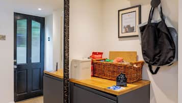 A hotel reception area with a black-framed mirror, a wicker basket with a sign, and a black bag hanging on the wall.