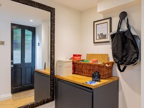 A hotel reception area with a black-framed mirror, a wicker basket with a sign, and a black bag hanging on the wall.
