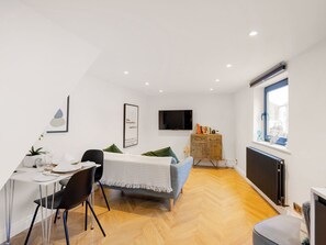 A modern bedroom with a bed, a TV, a wooden cabinet, and a dining area with chairs and a table.