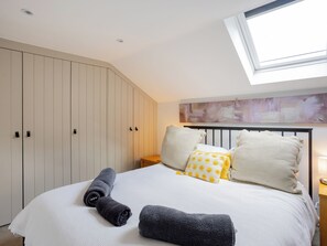 Un dormitorio con cama, almohadas, mesita de noche, armario y tragaluz.