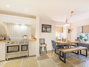 Una cocina moderna con horno empotrado, un área de comedor con mesa y sillas de madera, y una lámpara colgante.