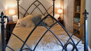 A bed with a diamond-patterned headboard, two bedside lamps, a heart-shaped wall decoration, and a wooden cabinet with towels.