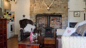 A cozy living room with a stone fireplace, a leather sofa, a wooden coffee table, and a dining table with glasses and a bottle.