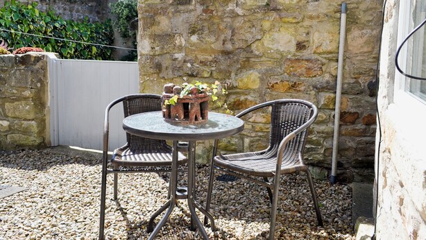 A stone wall with a small round table and two wicker chairs.