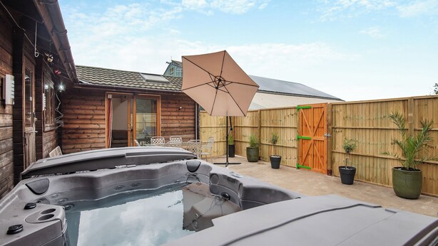 Un jacuzzi en un patio trasero con una cerca de madera, una casa de madera y un paraguas grande.