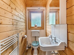 Een houten badkamer in een vakantiehuisje, met toilet, wastafel en raam.