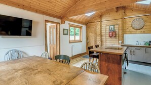Un interior de madera con una mesa de comedor, sillas, una zona de cocina con un fregadero y un reloj en la pared.