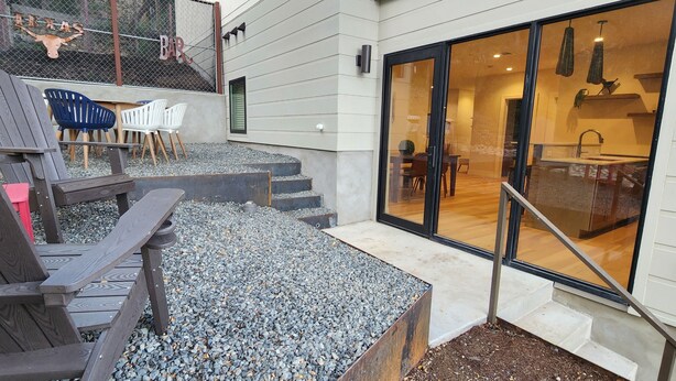 Een terras met buitenmeubilair, een trap die leidt naar een glazen deur en uitzicht op een modern interieur.