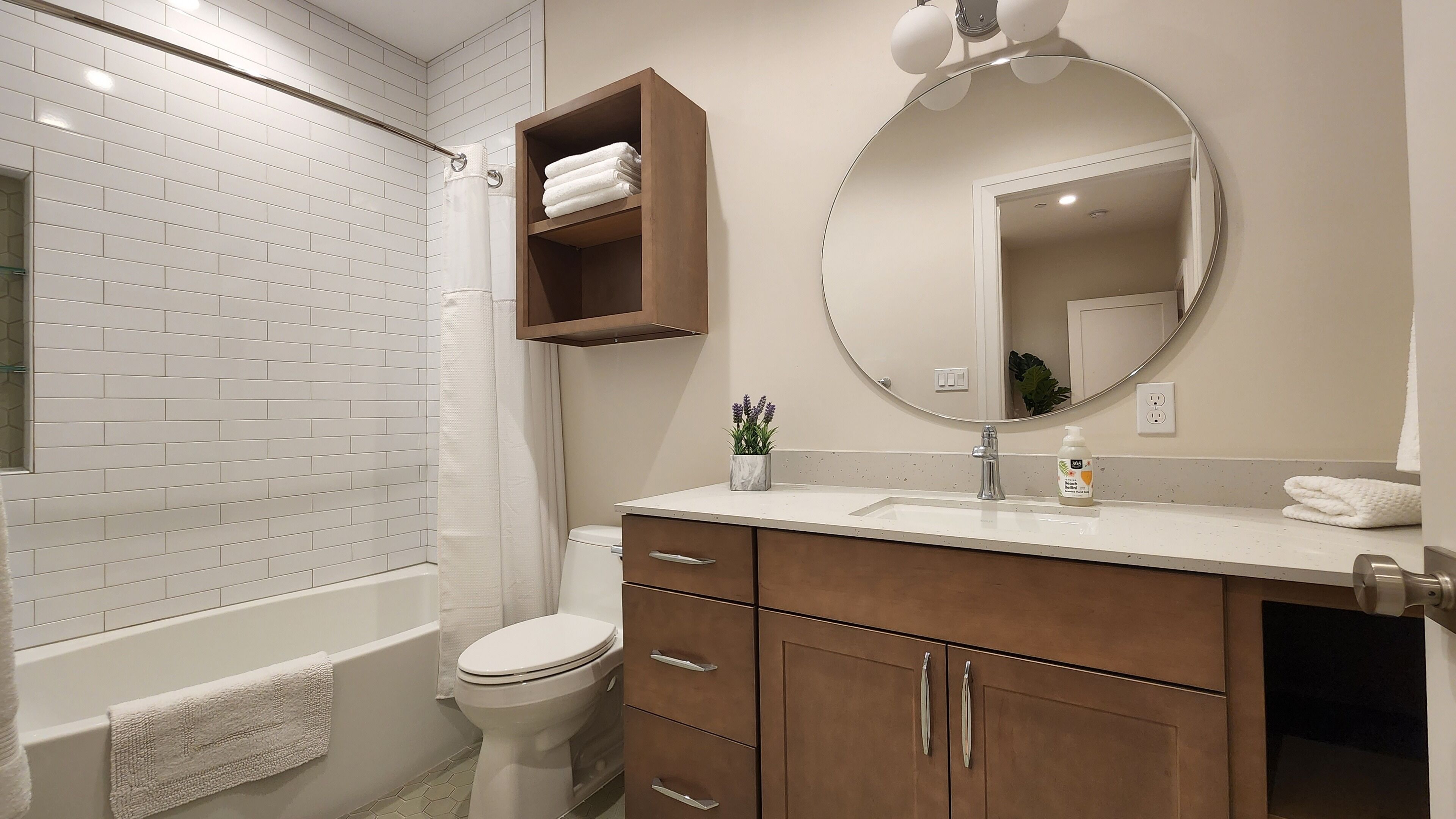 A modern bathroom with white subway tiles, a wooden vanity, a large mirror, and a shower area.
