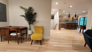 Een moderne woonkamer met een houten bureau, een gele stoel en een grote potplant.