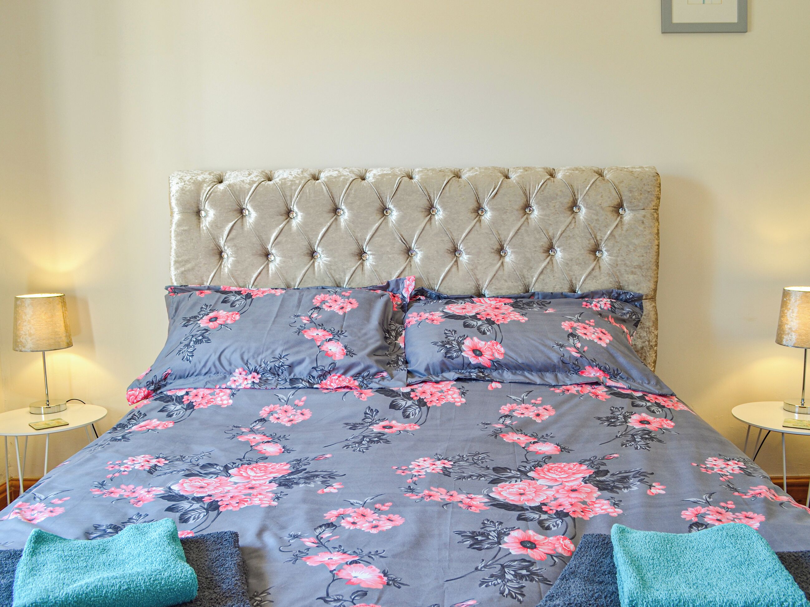 A bed with a tufted headboard, floral bedding, and two bedside lamps.