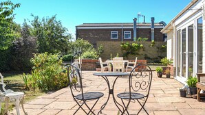 A patio with a table and chairs, surrounded by potted plants and a brick wall. - 4 bedroom accommodation in Hunstanton (Hunstanton)