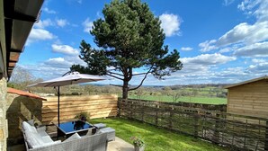 Une terrasse dotée de meubles en osier, d’une clôture en bois et offrant une vue sur la campagne.