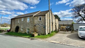 Un bâtiment en pierre avec un toit en pente, une cheminée bien visible et un petit jardin où poussent des jonquilles.