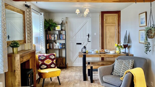 Un salon chaleureux avec une cheminée, une bibliothèque, une table à manger avec des chaises et un fauteuil confortable.