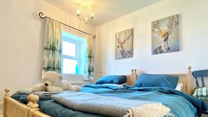 Une chambre à coucher avec un lit, une fenêtre avec des rideaux, un ours en peluche et deux tableaux accrochés au mur.