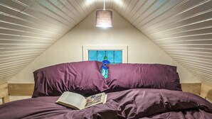 Un dormitorio con techo inclinado, una ventana con vistas y una cama con un libro.