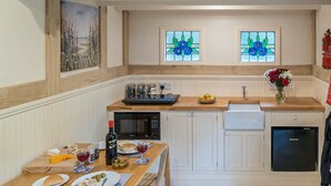 Una cocina compacta con armarios blancos, encimera de madera, una mesa de comedor con sillas, microondas, lavabo y lavavajillas.