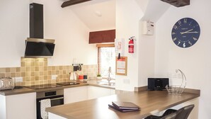 A modern kitchen with a central island, bar stools, a built-in oven, and a wall-mounted clock. - This delightful single storey cottage offers cosy holiday accommodation. (Kirkbymoorside)