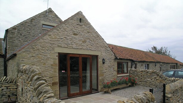 A stone house with a tiled roof, a wooden door, and a stone wall surrounding the property. - This delightful single storey cottage offers cosy holiday accommodation. (Kirkbymoorside)