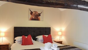 A hotel room with a large bed, two bedside lamps, a headboard, and a framed picture on the wall. - This delightful single storey cottage offers cosy holiday accommodation. (Kirkbymoorside)