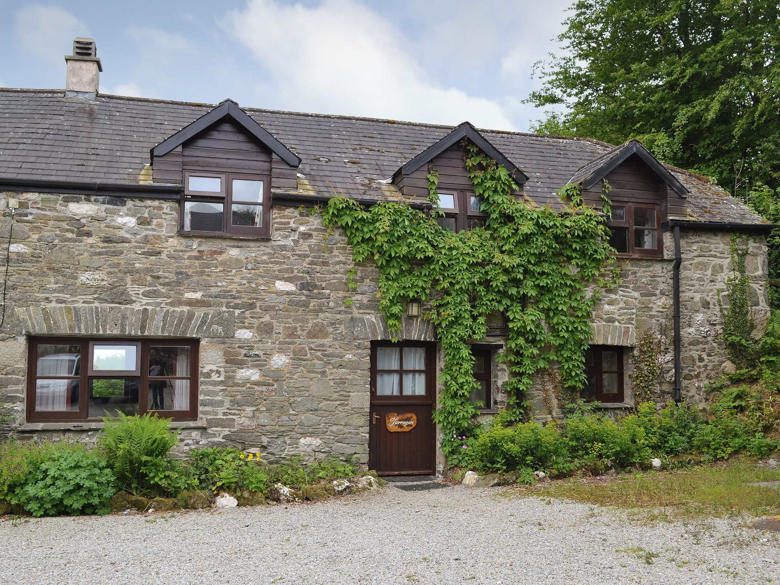 A stone building with multiple windows and a door, surrounded by greenery.