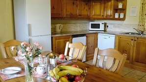 A kitchen with wooden cabinets, a refrigerator, a microwave, and a dishwasher. There is a dining table with chairs and a fruit bowl. - 3 bedroom accommodation in Dunterton, near Tavistock (Dunterton, near Tavistock)