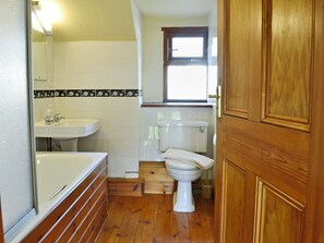 A compact bathroom with a wooden floor, white tiles, a white toilet, and a white sink. - 3 bedroom accommodation in Dunterton, near Tavistock (Dunterton, near Tavistock)