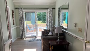 Ett vardagsrum med en soffa, en lampa och en skjutdörr i glas som leder ut till ett utomhusområde med stolar och ett bord.