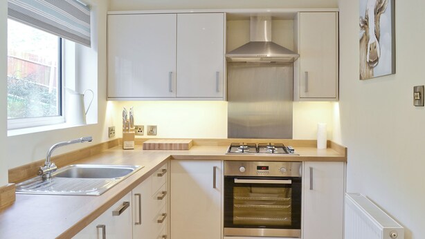 Een moderne keuken met witte kasten, een roestvrijstalen afzuigkap, een ingebouwde oven en een raam met zonwering.