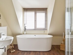 Ein modernes Badezimmer mit freistehender Badewanne, einem Waschbecken und einem Fenster mit Jalousien.