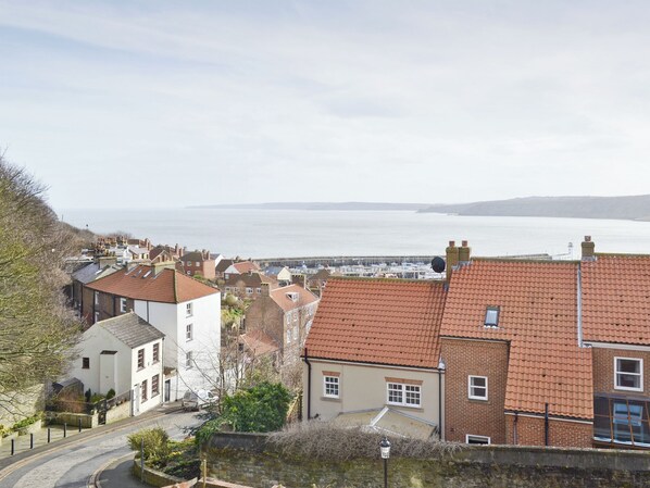 Eine Küstenstadt mit terrakottafarbenen Dächern, einer Steinmauer und Blick auf das Meer.