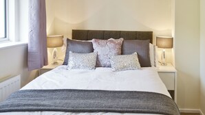 Een netjes opgemaakt bed met een grijze deken, een houten hoofdbord en twee bedlampen.