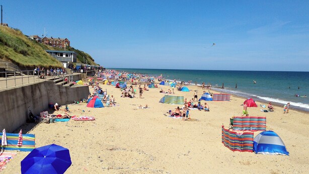 Een strand met tenten, parasols en mensen.