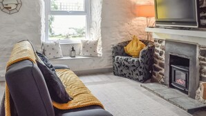 Un salon confortable avec un canapé, une cheminée, un téléviseur et une fenêtre donnant sur l’extérieur.