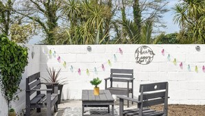 Un espace extérieur aménagé avec des bancs en bois et une table, le tout entouré d’un mur en briques blanches.