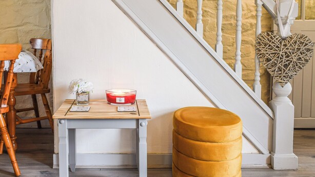Un escalier avec des balustrades blanches et une décoration en osier en forme de cœur. On peut voir une chaise en bois et une petite table sur laquelle est posée une bougie rouge.