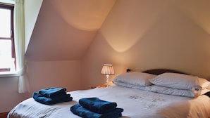 Un dormitorio con cama, mesita de noche, lámpara y ventana con cortinas.