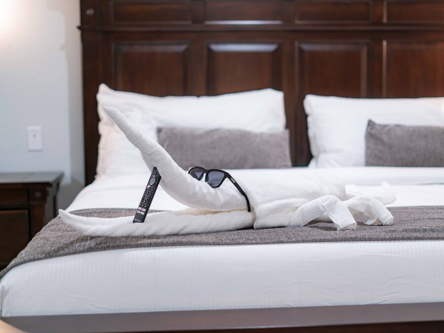 A neatly made bed with a remote control and sunglasses on the pillows.