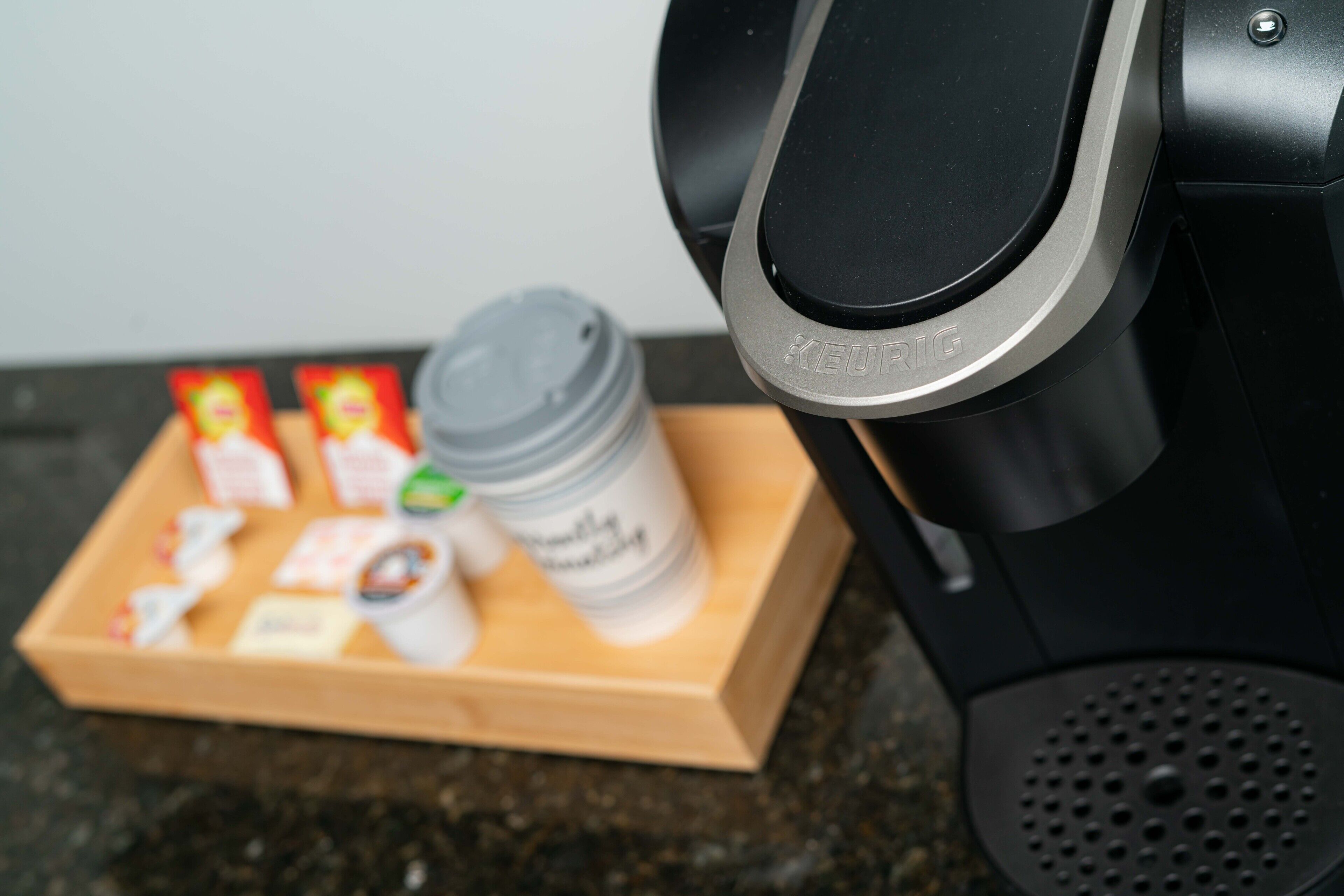 A Keurig coffee maker with a coffee pod and a cup on a wooden tray.